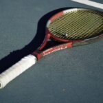 A high-quality tennis racket placed on a blue tennis court under sunlight.