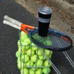 Outdoor tennis gear setup with rackets, balls, and a water bottle on a court.