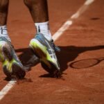 Tennis player in motion on a clay court in Paris, showcasing athletic shoes and dynamic movement.
